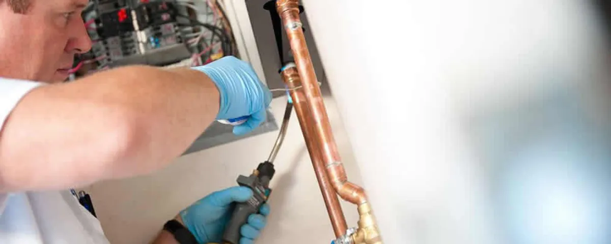 Water heater repair technician testing copper pipe connections and controls in Chandler, AZ
